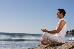 Young man meditating on a rock by the beach