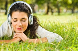 Young woman lying on grass listening to guided imagery on headphones